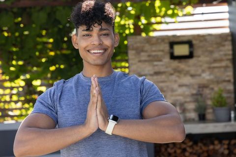 Young african man smiling pressing palms in namaste pose on sunny backyard patio