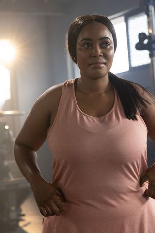 Confident african american woman standing hands on hips in gym wearing pink tank top