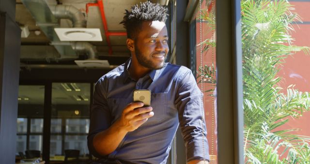 Businessman Smiling by Window Holding Phone in Modern Office - Download Free Stock Images Pikwizard.com