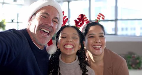 Multicultural family celebrating Christmas smiling for holiday selfie wearing Santa hat