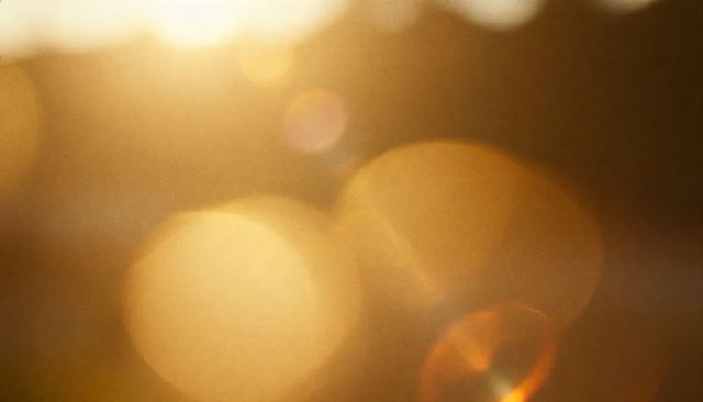 Golden sunset bokeh with large glowing orbs and warm lens flare for background