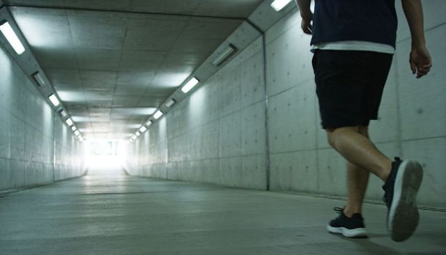 Man walking through concrete underpass toward bright exit with tube lights
