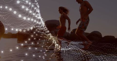 Young adults running on beach with glowing particles overlay