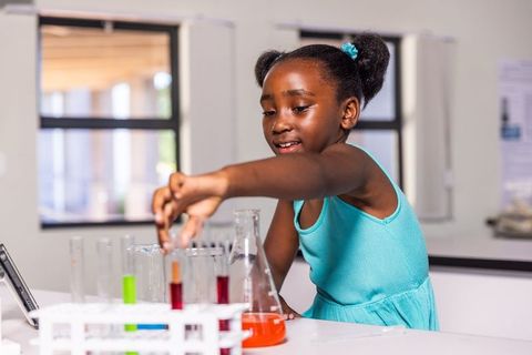 Young african american girl conducting colorful chemistry experiment in classroom lab