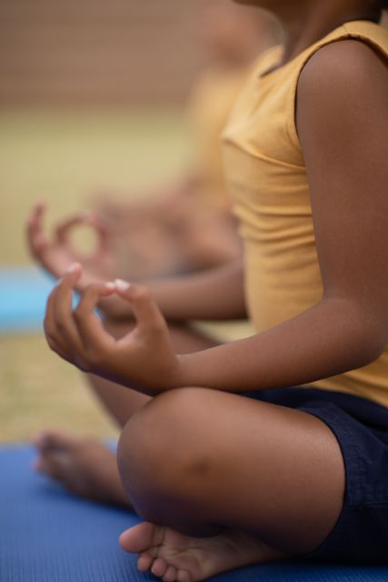 This image shows an African American schoolgirl meditating during a yoga class, focusing on mindfulness and relaxation. Ideal for use in educational materials, wellness programs, children's physical activity promotions, and articles on the benefits of yoga for kids.