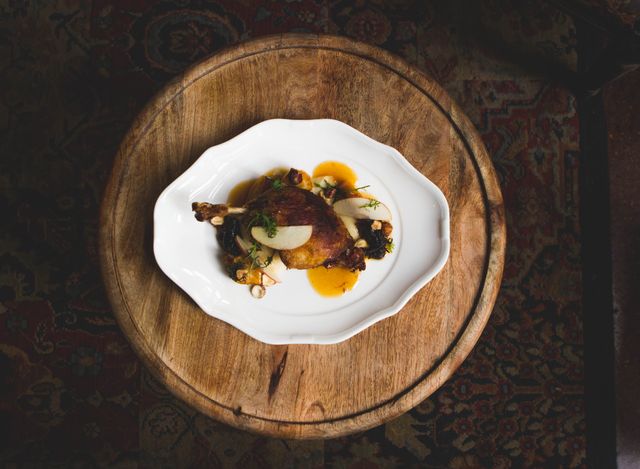 Delicious duck confit served on a classy plate placed on a rustic wooden table. The elegant presentation and dark lighting create a sophisticated ambiance. Ideal for use in culinary blogs, restaurant promotions, fine dining advertisements, or gourmet recipe collections.