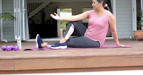 Woman performing seated spinal twist on outdoor yoga mat with dumbbells on wooden deck