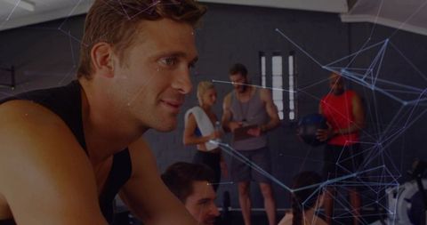 Fit man cycling on stationary bike pushing through sweat during group training