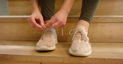 Tying sneaker laces on wooden steps, closeup wearing beige knit sneakers and olive leggings