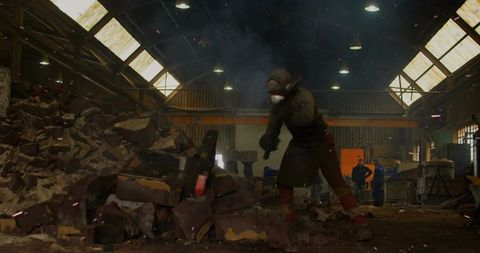 Industrial worker prying rubble in gritty warehouse wearing helmet mask apron gloves boots