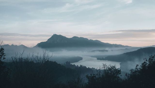 Misty mountain dawn with jagged summit and winding river in serene foggy valley panorama