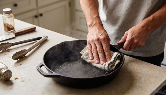 Seasoning cast-iron skillet using cloth while steam rising on home kitchen counter