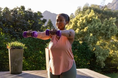 Woman exercising with dumbbells outdoors amid scenic greenery