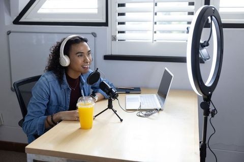 Non-binary creator recording podcast using condenser microphone, ring light, laptop