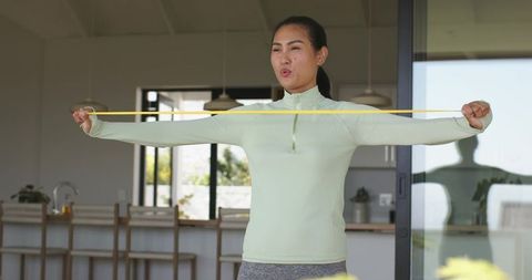 Asian woman stretching with resistance band in sunlit open-plan kitchen for home workout