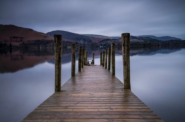 Rustic wooden pier on calm lake with mountains in background - Download Free Stock Photos Pikwizard.com