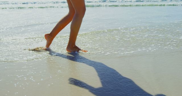 Barefoot woman walking on sandy beach with ocean waves in the background, suggesting leisure and relaxation. Ideal for travel advertisements, summer vacation promotions, wellness blogs, and tourism brochures.