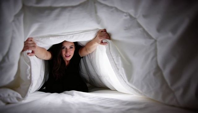 Woman peeking through white duvet pulling comforter tunnel, cozy intimate bedroom portrait