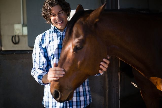 Smiling man caressing the brown horse in the ranch