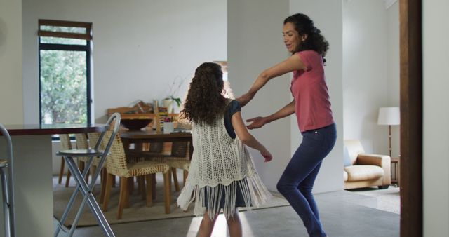 A mother and her daughter are happily dancing together in their living room. Ideal for depicting family bonding, happiness, and joyful home activities. This can be used in articles or advertisements about family life, parenting, or indoor activities.