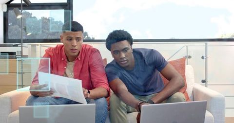 Two men collaborating on laptops in bright modern home office reviewing documents