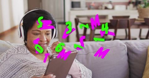 Senior woman relaxing on sofa holding tablet listening with headphones and neon doodles
