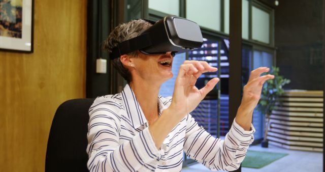 Ideal for illustrating modern technology usage in office environments, this image shows a woman interacting with virtual reality while wearing a VR headset. Can be used for articles on technological advancements, workplace innovations, or the future of remote work and employee training.