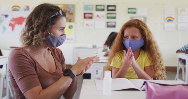 Teacher and student wear face masks while practicing hand hygiene in a classroom. Capture highlights safe learning environment during pandemic. Useful for topics covering pandemic education protocols, health safety measures, or return to school initiatives.