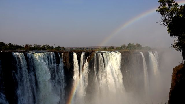 This captivating image captures the powerful cascading waters of Victoria Falls complemented by a stunning natural rainbow. Ideal for travel blogs, tourism websites, nature documentaries and educational content.