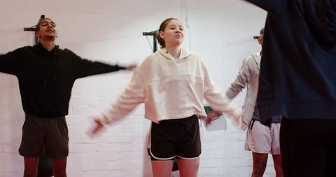 Diverse group warming up and stretching arms while bending sideways in gym class