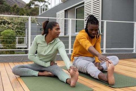 Indian woman and african american man stretching on deck yoga mats during outdoor workout