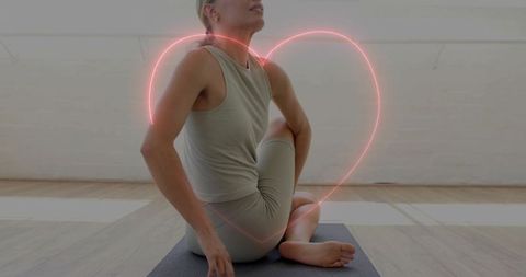 Seated spinal twist in beige activewear framed by neon heart for mindful self-love
