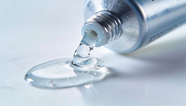 Macro close-up of clear gel dispensing from metal tube showing bubbles and reflection