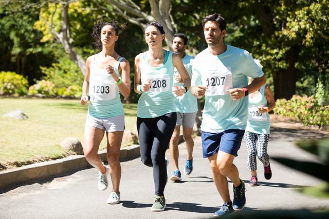 Group of marathon athletes running in a leafy park on a sunny day. They are all wearing race numbers and athletic wear, showing determination and focus. Great for illustrating concepts of fitness, strength, determination, and teamwork.