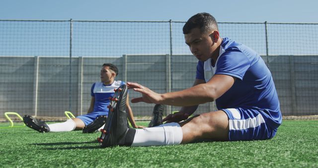 Soccer players in blue uniforms stretching on green turf before practice. Useful for sports training programs, fitness promotions, athletic gear advertisements, and educational materials on the importance of warm-up exercises in sports.