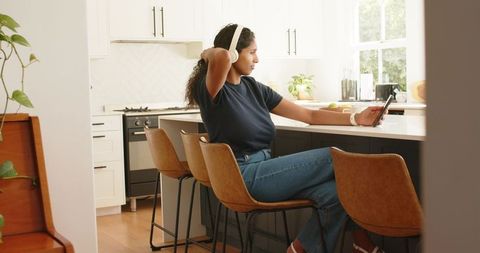 African american woman relaxing with headphones and smartphone at modern kitchen island