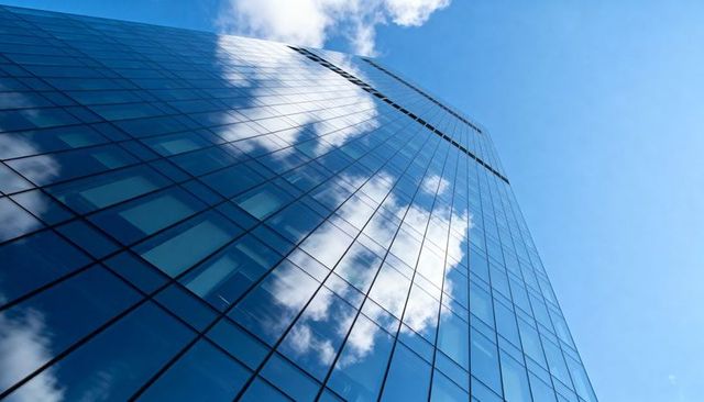 Modern Glass Facade Skyscraper Reflecting Blue Sky and Clouds Vertical Upward Perspective