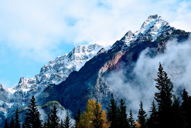 Depicting majestic snow-capped mountain peaks shrouded in light mist, with a tranquil forest in the foreground. Captures the serene beauty of nature and the great outdoors. Suitable for use in travel promotions, nature-themed projects, environmental campaigns, and landscape photography displays.