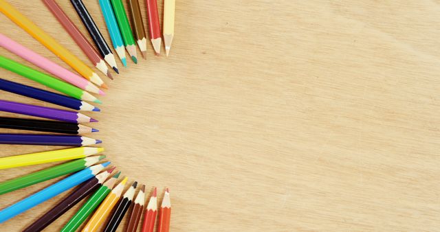 Colored pencils are arranged in a semi-circle on a wooden surface, with copy space. This arrangement is often associated with creativity, education, and artistic pursuits.