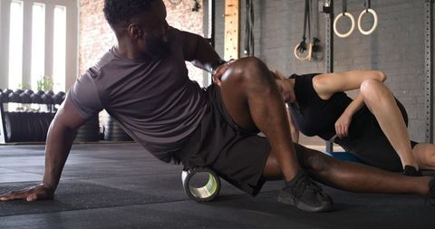 Diverse workout partners practicing foam rolling therapy