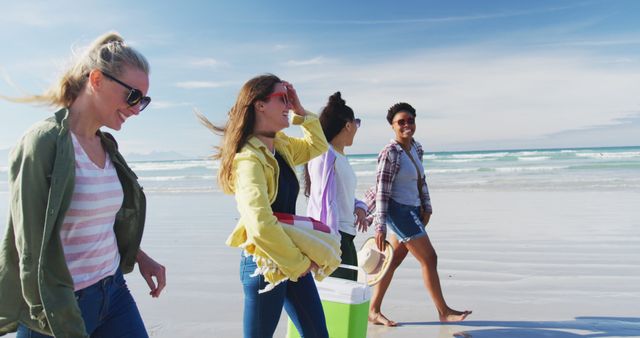 Group of friends walking on a sandy beach on a sunny day. Perfect for marketing travel destinations, vacation packages, summer fashion, and lifestyle blog posts. Captures the essence of outdoor fun and social activities.