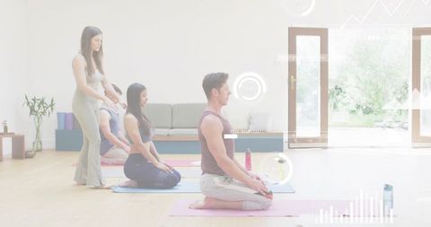 Adults practicing yoga kneeling sunlit studio instructor adjusting posture alignment breathing