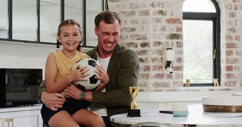 Smiling Father and Daughter with Soccer Ball in Kitchen
