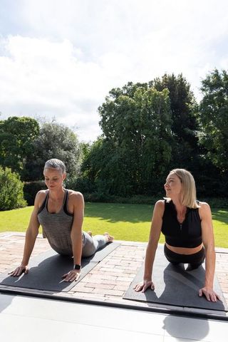 Senior women practicing backbend on patio yoga mats with smartwatch in garden
