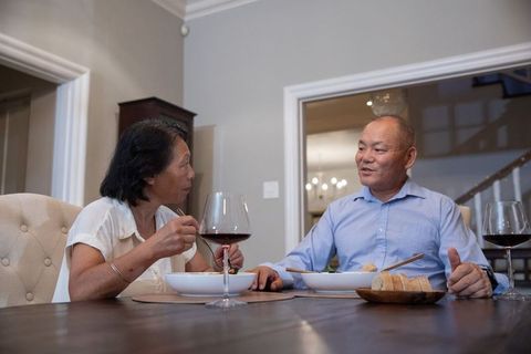 Asian senior couple sharing intimate dinner with wine and bread in cozy home dining room