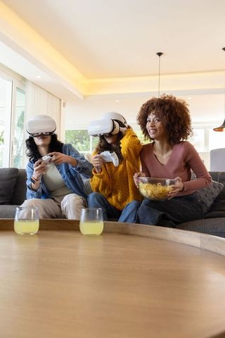 Diverse friends playing virtual reality games on sofa sharing snacks and laughing together