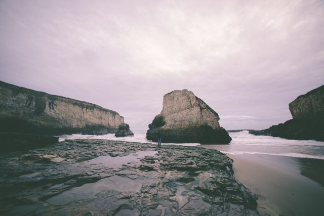 This image captures a tranquil coastal landscape with rocky cliffs and an overcast sky. The waves gently crash against the shore, creating a serene atmosphere. Ideal for promoting travel destinations, nature blogs, or environmental campaigns focusing on coastal conservation.