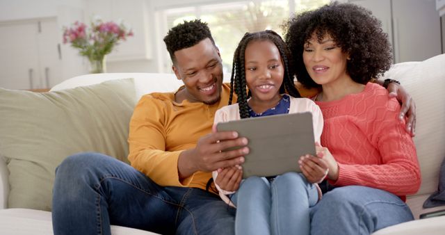 Happy african american parents with daughter using tablet at home. Domestic life, family, technology and lifestyle, unaltered.