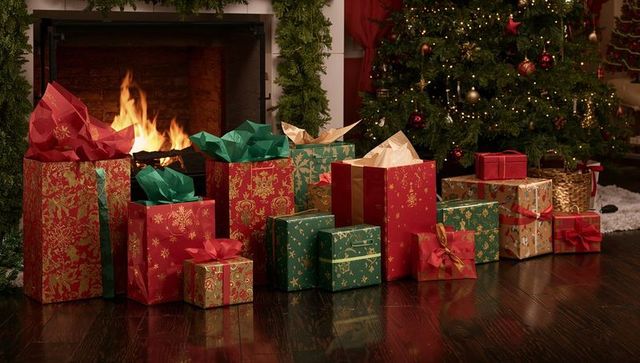 Holiday gifts by fireplace with decorated christmas tree, garland, ornaments and warm hearth