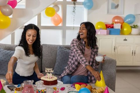 Multicultural friends decorating living room for birthday party, laughing and celebrating